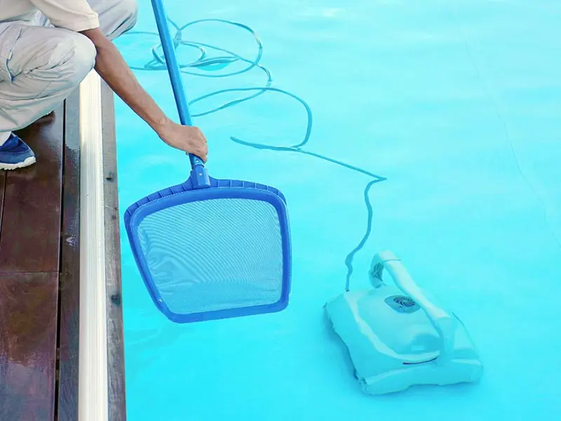 Profissional da Manancial Piscina fazendo a limpeza da superfície da piscina